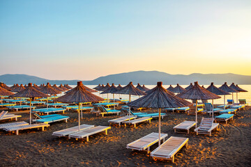 Straw umbrellas and sunbeds on the beach against the background of the sea in the morning