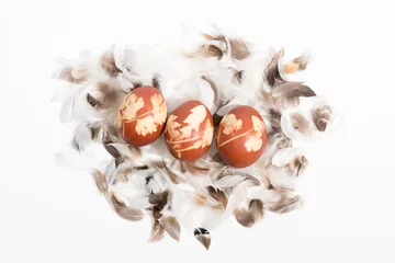 Fototapeten Gekochte Eier mit Zwiebelschalen gefärbt, mit Mustern von Gräsern und in Batikmanier, auf kleinen Federn liegend. © Christine