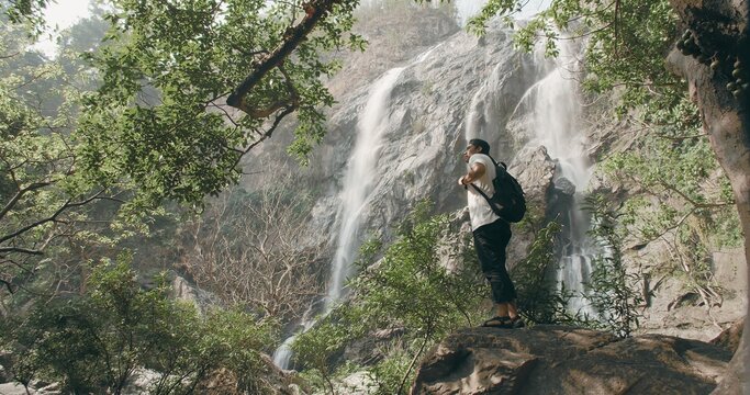 A man is standing on a rock near a waterfall