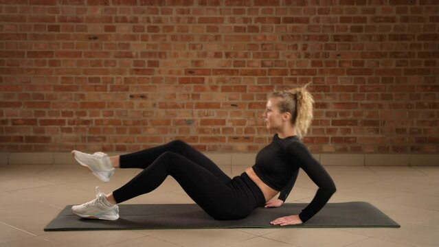 A professional trainer performs a right leg single-leg V-tuck, targeting the core for improved muscle coordination and fitness in a minimalist gym setting. Camera 8K RAW. 
