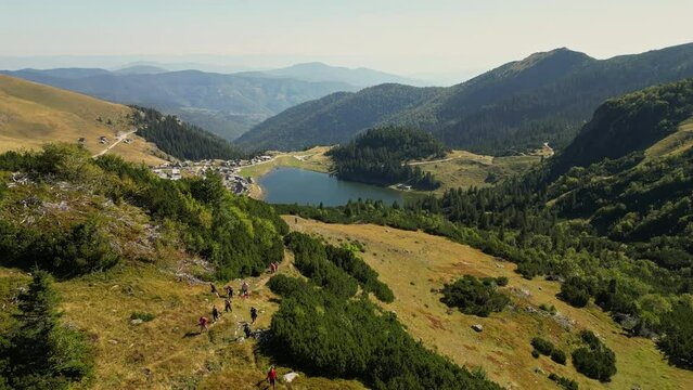 Aerial View of a Group of People Hiking and Leaving a Scenic Mountain Village with a Lake Behind. Concept of healthy life, excursion, trekking, backpacking, enjoying the nature. Mount Vranica, Bosnia