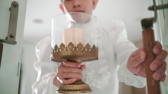 Altar boy in white robe holding a lit candle in a decorative lantern, preparing for a religious ceremony in a church.