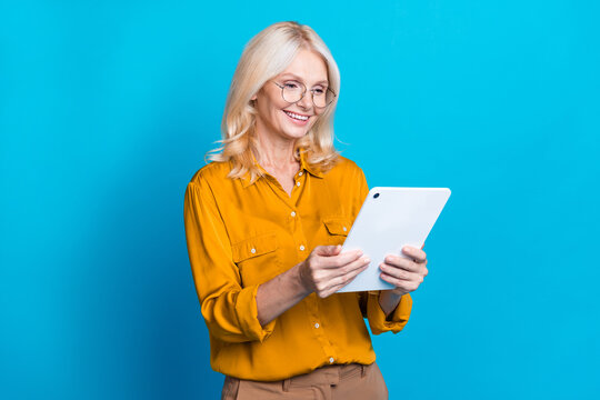 Photo portrait of pretty pensioner female ebook manager agent dressed stylish orange smart casual outfit isolated on blue color background - Powered by Adobe