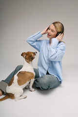 Girl and pet music lover. Blonde woman sitting on the floor with black headphones listening to song cute white dog looking at her with love. Studio shot. Gray and blue colors