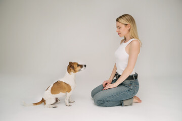 dog and a girl are sitting on the floor opposite each other and looking at each other. Adorable team studio shoot. Grey background