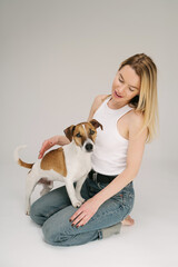 Blond woman sitting on floor and looking at small white dog Jack Russell terrier. Studio shot. Cute friends portrait. Dog owner care