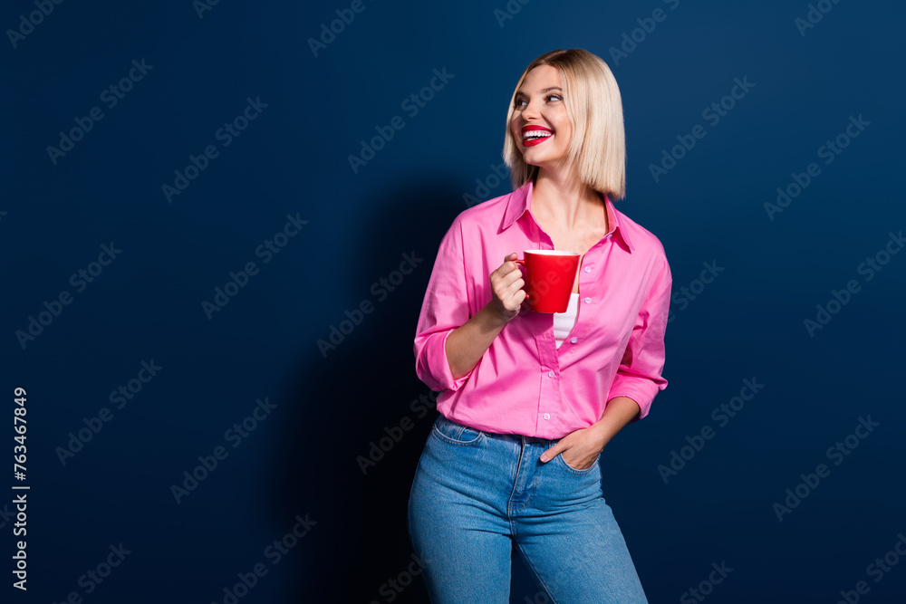 Sticker Photo of optimistic girl dressed pink shirt hold cup of drink look at tea shop logo empty space isolated on dark blue color background