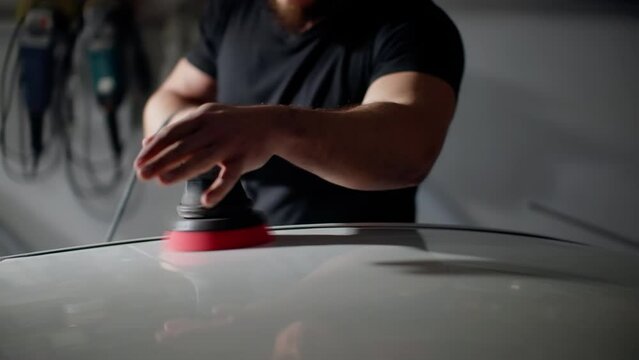 Focused Craftsman Polishing Car with Buffer, Soft Background Blur of Garage Workspace
