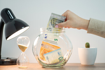 Saving money in Europe concept. Woman putting 5 euro banknote to jar