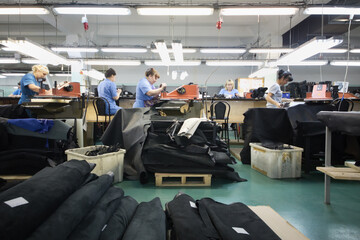 six woman in workshop with leather and suede cutting machines in factory.