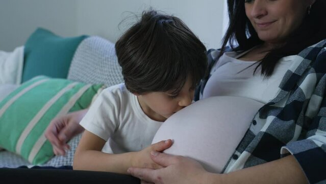 Boy's Loving Kiss to Unborn Brother, Tender Moment with Pregnant Mother on Home Couch. Third trimester of pregnancy, maternal concept