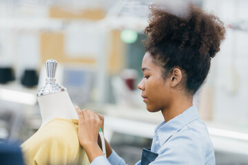 Close-up of working and designing clothes from an American female designer in a sewing factory using a sewing machine on a mannequin with a measuring tape and expert skills.