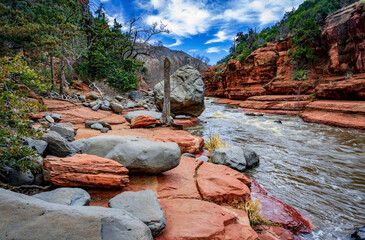 A large gray boulder and other gray rocks next to Oak Creek in Arizona's red rock country - 763485276