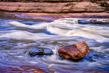 Gray and red boulders in the rushing water of Oak Creek near Sedona Arizona - 763485295