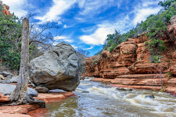 A large gray boulder sits next to Oak Creek in Arizona's red rock country