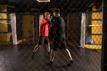 Two young professional boxer boxing in gym cage.