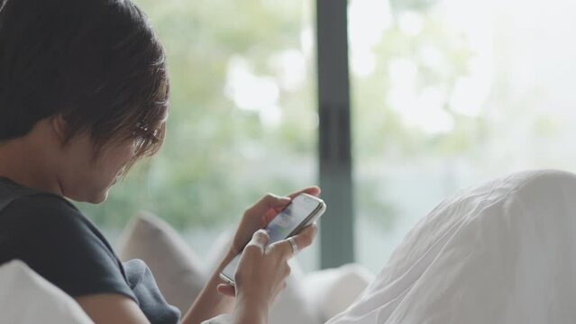 Close up face of pretty asian woman who is using smartphone for online socialising and communicating with morning sunlight in the bed shows concept of relaxation and comfort for refreshing.