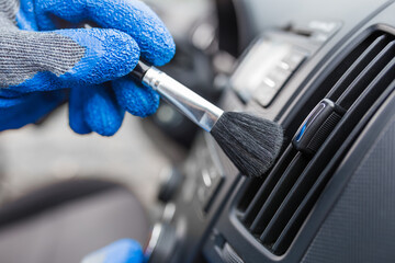 Man hands using cleaning brush and removing dust from car air conditioning vent grill. Car...