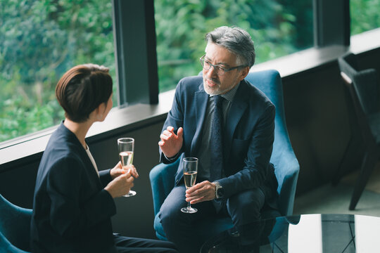 ラウンジでシャンパンを飲むシニア経営者と秘書
