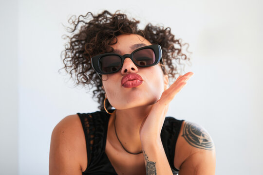 jeune femme mannequin envoyant des baisers, portant des lunettes de soleil noires, la main sur le menton, posant pour la photo, sur fond blanc dans le style de la photographie de mode
