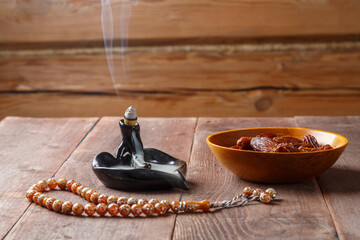 On the table are steaming incense, dates and Ramadan rosaries