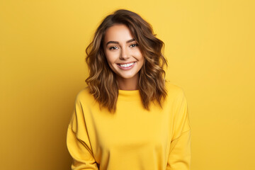 Portrait of a smiling young woman over yellow background. Young woman cute face expression posing in yellow hoodie on yellow background. - 763503607