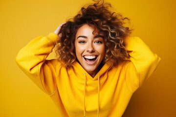 Portrait of a smiling young woman over yellow background. Young woman cute face expression posing in yellow hoodie on yellow background. - 763503608