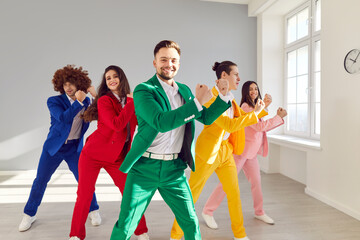 Portrait of happy cheerful dancers moving in bright suits together enjoying disco party. Five young funny friends dancing indoors in colorful fashionable costumes in dance studio indoors.