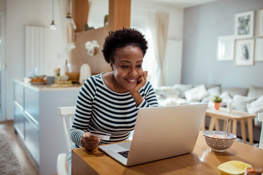 Smiling woman with credit card looking at laptop in home