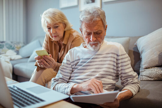 Senior couple reviewing documents and using smartphone on couch at home
