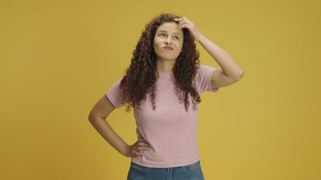 Pensive young woman 20s years old in pink t-shirt posing looks around thinks scratches at temple comes up with ideas raised finger up isolated on yellow background in studio. People lifestyle concept
