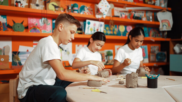 Group of happy smart diverse student working with clay art at pottery workshop. Multicultural attractive highschool student modeling, smash, playing clay. Creativity activity concept. Edification.