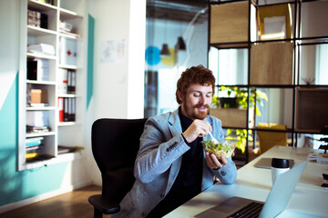 Young businessman eating a salad in the modern office