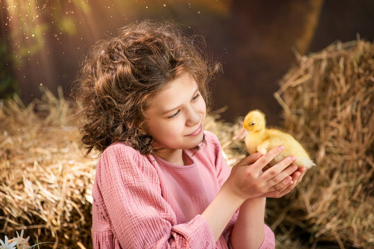 A young girl is holding a duckling in her arms.