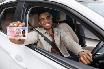  Happy young african man showing his driver's license from open car window - obrazy, fototapety, plakaty