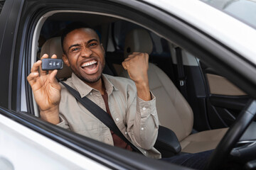 Joyful african american guy holding auto key shaking fists sitting in automobile 