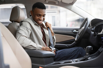 African American man sitting in a car in a car dealership fastening his seat belt - obrazy, fototapety, plakaty
