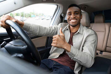 Young african american man smiling while driving a car showing thumbs up recommending something good.