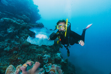 A woman in a black wetsuit is swimming in the ocean and pointing at a jellyfish