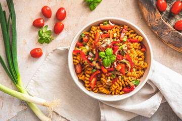 Pasta salad with pepper, tomatoes, spring onions and basil in a white bowl on light background, top view