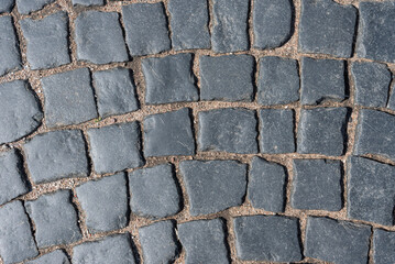 The texture of a paved road made of dark gray smooth and uneven cobblestones