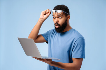Attractive, excited African American man wearing stylish eyeglasses, holding laptop, using computer