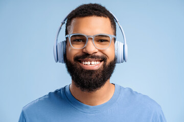 Handsome, smiling African American man wearing headphones and stylish eyeglasses, listening to music
