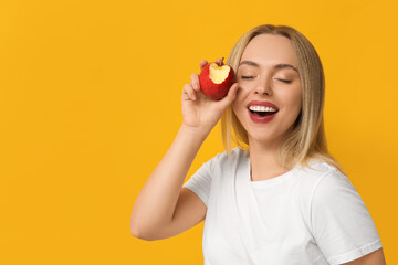 Young woman eating apple on yellow background, closeup