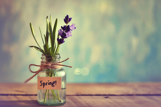 Spring flowers in a glass bottle on a wooden table and green background