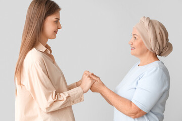 Mature woman after chemotherapy with her daughter holding hands on light background. Stomach cancer concept