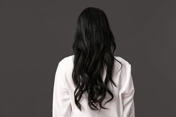 Beautiful young woman with dark wavy hair in white blouse on black background, back view