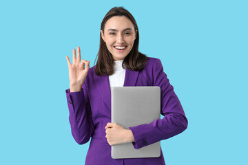 Young businesswoman with laptop showing OK gesture on blue background