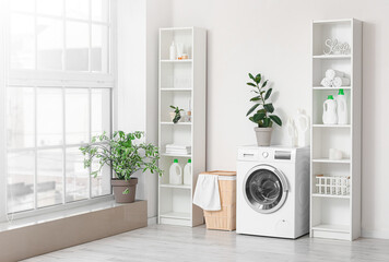 Modern washing machine with basket and shelving units near white wall. Interior of home laundry room