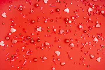 Sweet colorful sprinkles scattered on red background